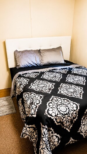 A bed with a white headboard, a black and white patterned bedspread, and a grey pillow. - 2-bedroom mobile home in fantastic Hartwell with free space for boat rv parking  (Hartwell)
