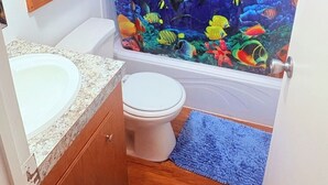 Ein Badezimmer mit Duschvorhang mit Unterwasser-Motiv, Toilette, Waschbecken und einem Holzregal mit Handtüchern.