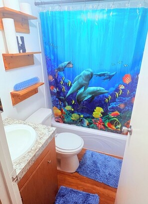 A bathroom with a shower curtain depicting an underwater scene, a toilet, a sink, and a wooden shelf with towels. - 2-bedroom mobile home in fantastic Hartwell with free space for boat rv parking  (Hartwell)