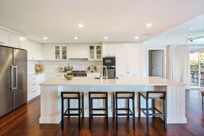A modern kitchen with white cabinetry, a large island with bar stools, stainless steel appliances, and a view to the outdoors.