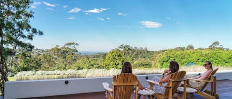 Une terrasse en bois avec deux chaises en bois et une petite table, offrant une vue panoramique sur un paysage verdoyant, avec des arbres et un ciel dégagé.