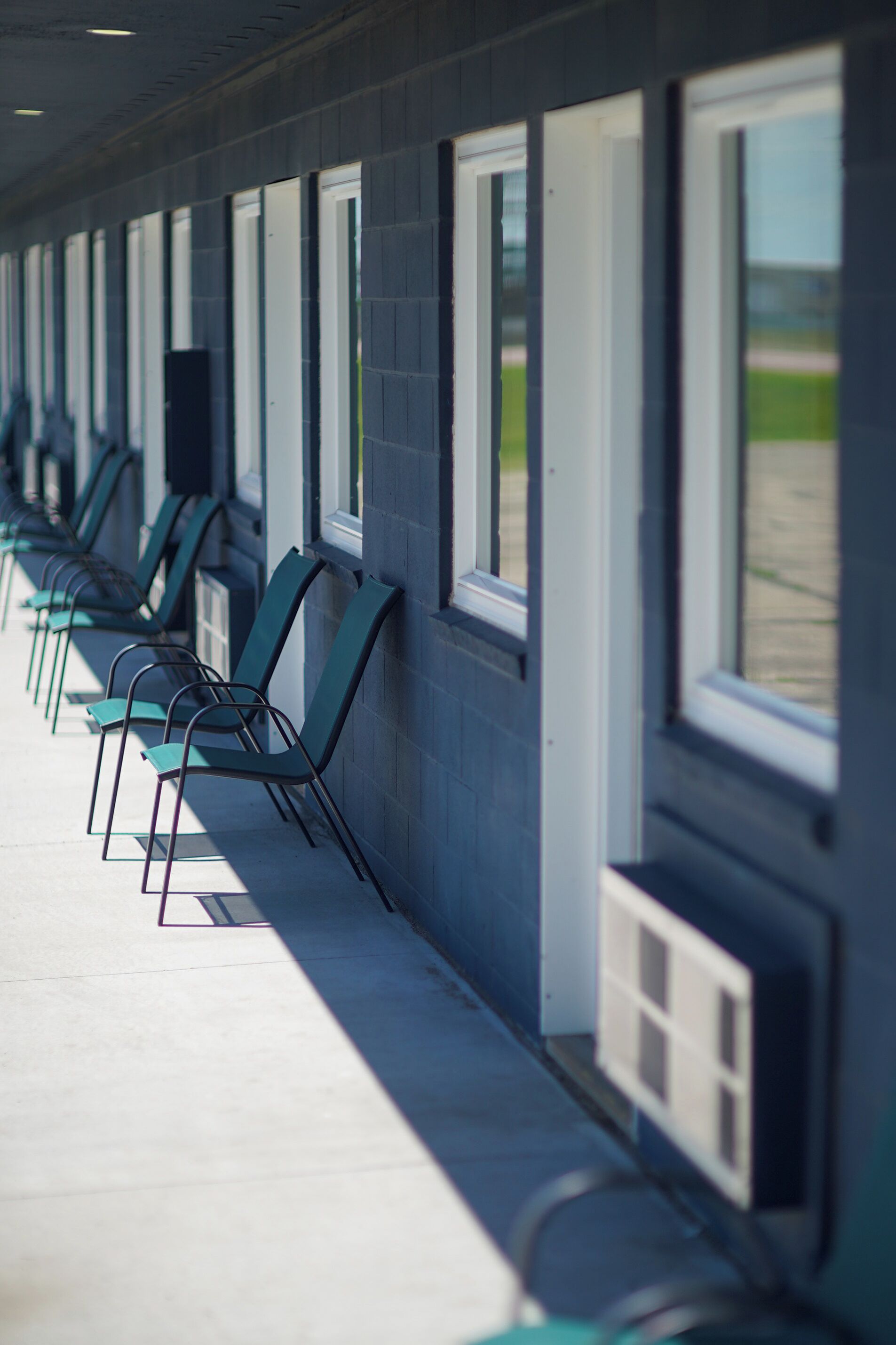 A row of green chairs aligned against a building wall with windows.