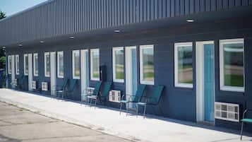 A building with a row of windows and doors, outdoor seating with chairs, and a clear sky.