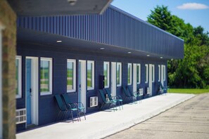 A row of single-room cabins with a flat roof and large windows, arranged along a paved walkway.
