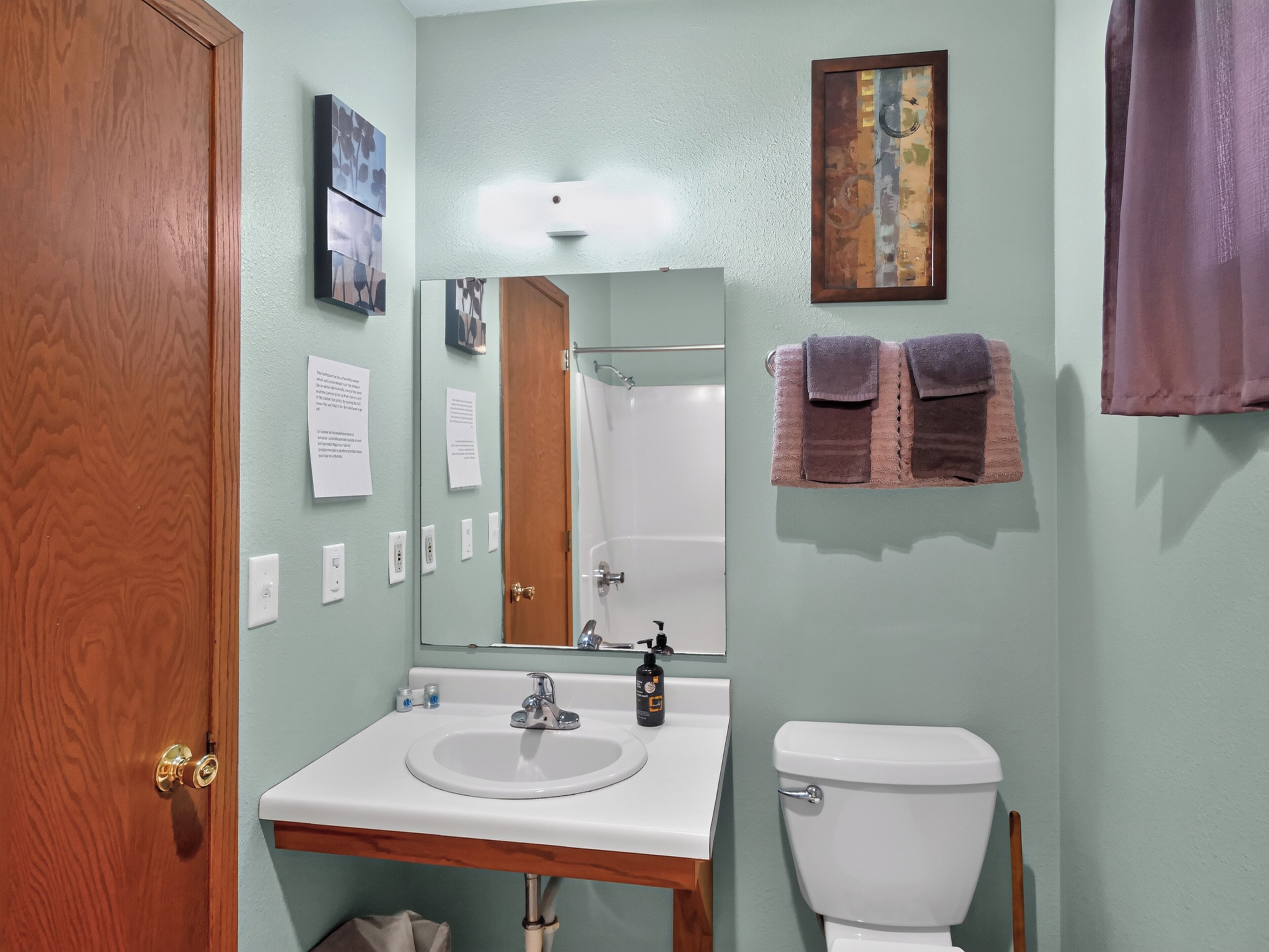 Une salle de bain avec une porte en bois, un lavabo blanc, un miroir et des toilettes.