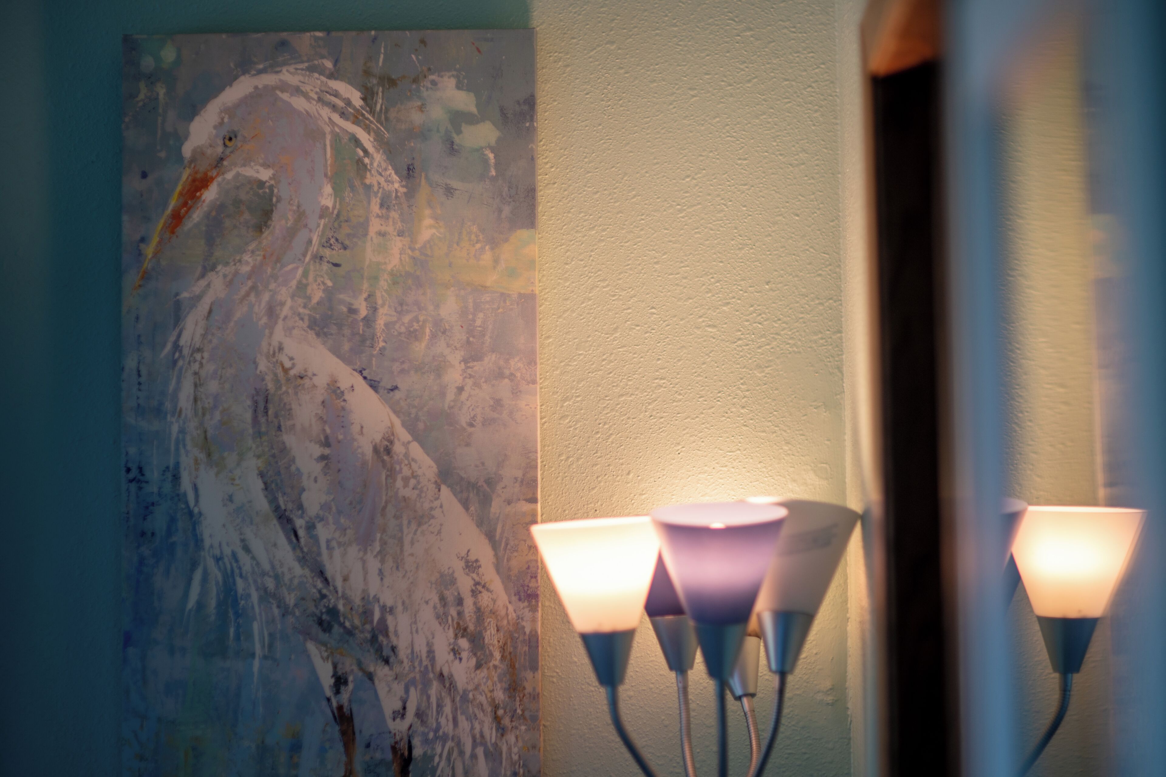 A wall with a painting of a bird and a modern light fixture.