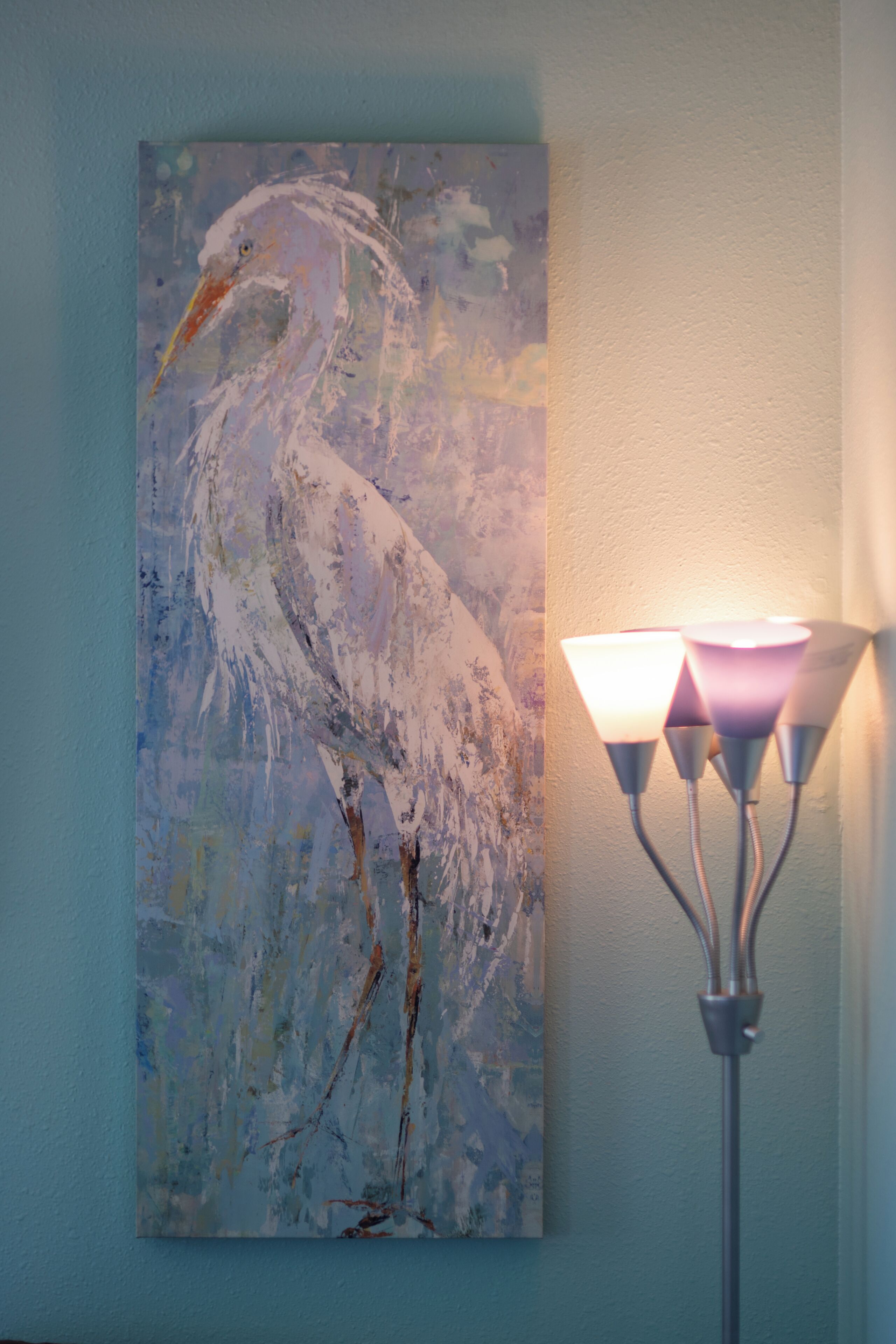 A painting of a bird on a wall, next to a lamp.