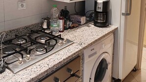 A compact kitchen with a built-in microwave, a gas stove, a coffee maker, and a washing machine.
