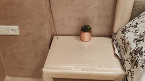 A small bedside table with drawers, a potted plant, and a wall socket.