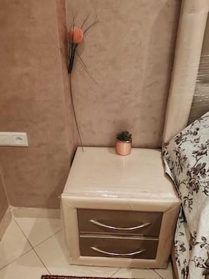 Une petite table de chevet avec des tiroirs, une plante en pot et une prise électrique murale.