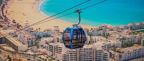 Un teleférico sobre una ciudad costera con playa y edificios residenciales.