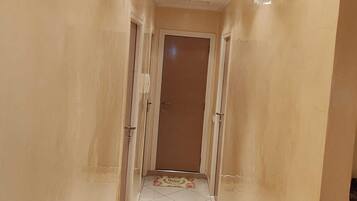 A hallway with a tiled floor, a door at the end, and recessed lighting on the ceiling.