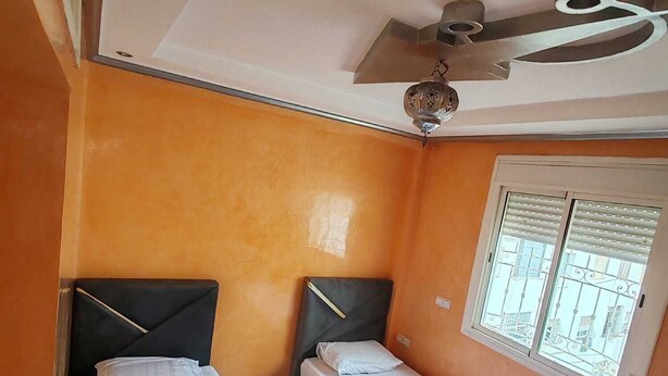 A small room with two beds, a ceiling fan, and a window with bars.