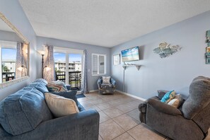 A living room with a sofa, armchair, and a TV on the wall. - Perfect Gulf Shores Getaway With Pools, Hot Tubs and Beach Access (Gulf Shores)