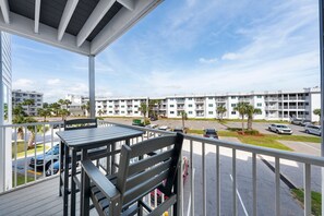 A balcony with a table and chairs, overlooking a parking lot and a row of white buildings with balconies. - Perfect Gulf Shores Getaway With Pools, Hot Tubs and Beach Access (Gulf Shores)