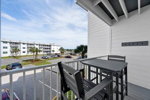 A balcony with a table and chairs, overlooking a parking lot and a building with multiple floors. - Perfect Gulf Shores Getaway With Pools, Hot Tubs and Beach Access (Gulf Shores)