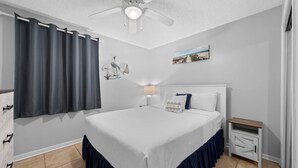 Un dormitorio con cama, mesita de noche, ventilador de techo e imagen colgada en la pared.