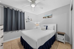 Ein Schlafzimmer mit Bett, Nachttisch, Deckenventilator und einem an der Wand hängenden Bild.