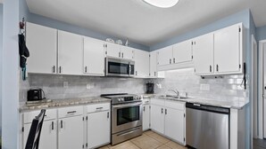 Una cocina moderna con armarios blancos, electrodomésticos de acero inoxidable y salpicadero de azulejos.