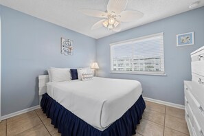 A bedroom with a bed, a ceiling fan, a window with blinds, a dresser, and a wall decoration. - Perfect Gulf Shores Getaway With Pools, Hot Tubs and Beach Access (Gulf Shores)