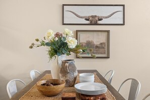 A dining table set with white plates, a wooden bowl, a ceramic pitcher, and a vase with flowers. - 6BR Aggie Compound Near A&M • 2 Kitchens & 6 Cars (College Station)