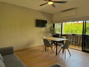 Ein modernes Wohnzimmer mit Holzboden, Deckenventilator, flachbildfernseher an der Wand und einem Essbereich mit Tisch und Stühlen.