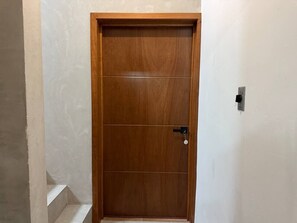 Eine Holztür mit Schlüsselloch und Schloss, in eine schlichte Wand eingelassen, mit sichtbarer Steckdose.