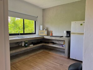 Eine kompakte Küche mit eingebautem Spülbecken, einer Mikrowelle, einer Kaffeemaschine und einem Kühlschrank.