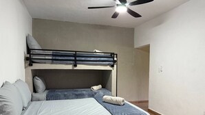 Un dormitori amb una llitera, un llit individual, un ventilador de sostre i una porta visible que dona a una altra habitació.