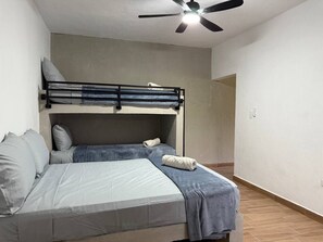 Ein Schlafzimmer mit Etagenbett, einem Einzelbett, Deckenventilator und einer sichtbaren Tür zu einem anderen Raum.