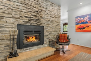 A fireplace with a stone wall, a leather chair with a blanket, and a painting on the wall. - Modern Mountain Retreat - 4-bedroom, family friendly, peaceful (Durango)