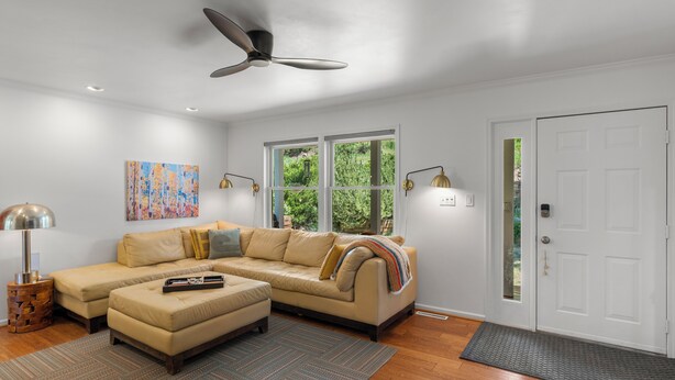 A modern living room with a beige sectional sofa, a small coffee table, a ceiling fan, and a large window with a view of greenery. - Modern Mountain Retreat - 4-bedroom, family friendly, peaceful (Durango)