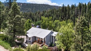 A two-story house with a deck, surrounded by dense forest and mountains in the background. - Modern Mountain Retreat - 4-bedroom, family friendly, peaceful (Durango)