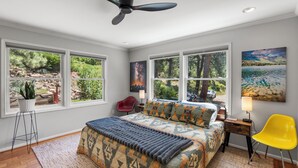 A bedroom with a bed, a red chair, a yellow chair, a ceiling fan, and large windows with a view of greenery. - Modern Mountain Retreat - 4-bedroom, family friendly, peaceful (Durango)