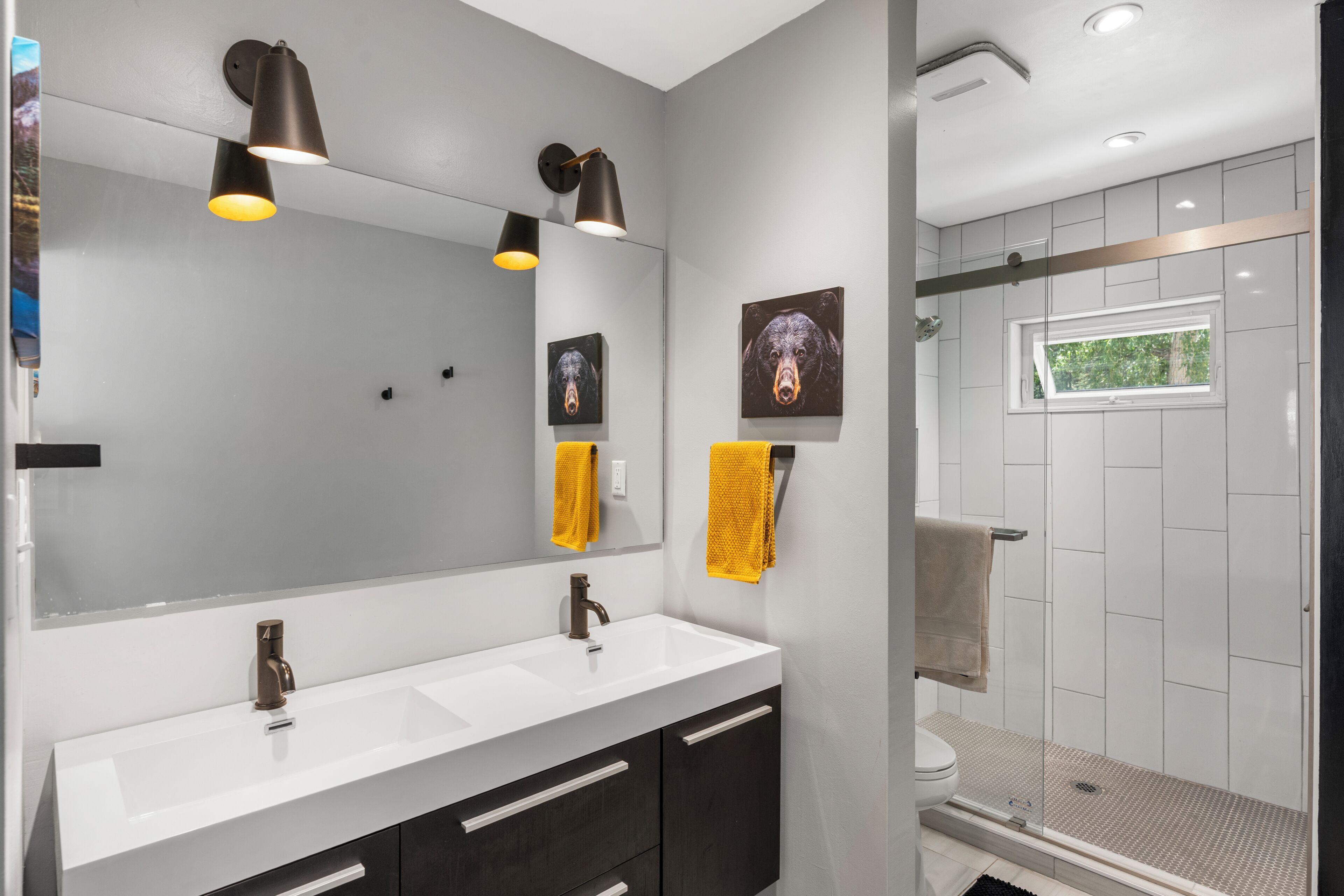 A modern bathroom with a dual sink vanity, a large mirror, and a glass-enclosed shower.