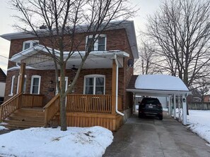 A two-story brick house with a covered porch and a garage. - Cozy 2-bedroom basement in Peterborough (Peterborough)