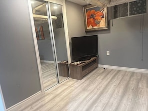 A room with a flat-screen TV on a wooden stand, a large mirror, and a painting on the wall. - Cozy 2-bedroom basement in Peterborough (Peterborough)