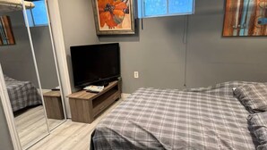 Een slaapkamer met een bed, een televisie, een dressoir en een spiegel.