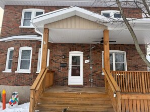 A two-story brick house with a wooden front porch, a white door, and a mailbox.