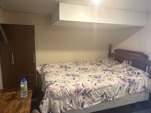 A bedroom with a bed, a wooden wardrobe, and a water bottle on a wooden table. - Cozy 2-bedroom basement in Peterborough (Peterborough)
