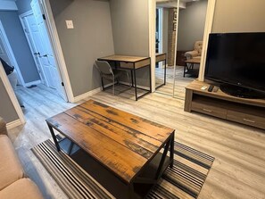 A living room with a wooden coffee table, a TV stand, a sofa, and a dining area with a table and chairs. - Cozy 2-bedroom basement in Peterborough (Peterborough)