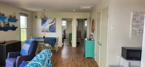 A room with a dining table, chairs, a sofa, a television, and a kitchen area. - Seaside Cottage just minutes from the beach! (Kensington)