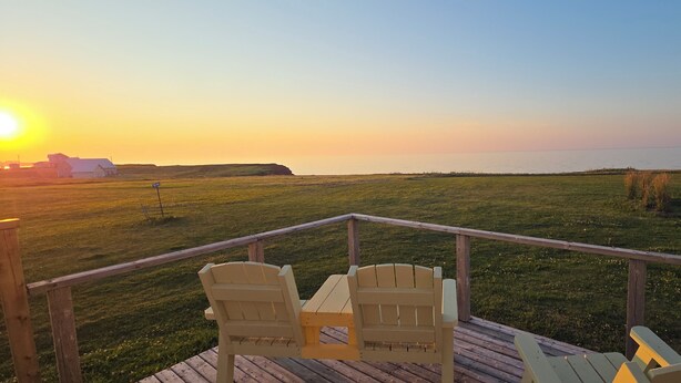 Une terrasse avec deux fauteuils Adirondack donnant sur un champ verdoyant et un coucher de soleil.