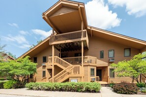 A two-story building with a wooden exterior, a balcony on the upper floor, and a staircase leading to the entrance. - New rental 3 bedroom 3 full bath condo at Shanty Creek Resorts golf boat parking (Mancelona)