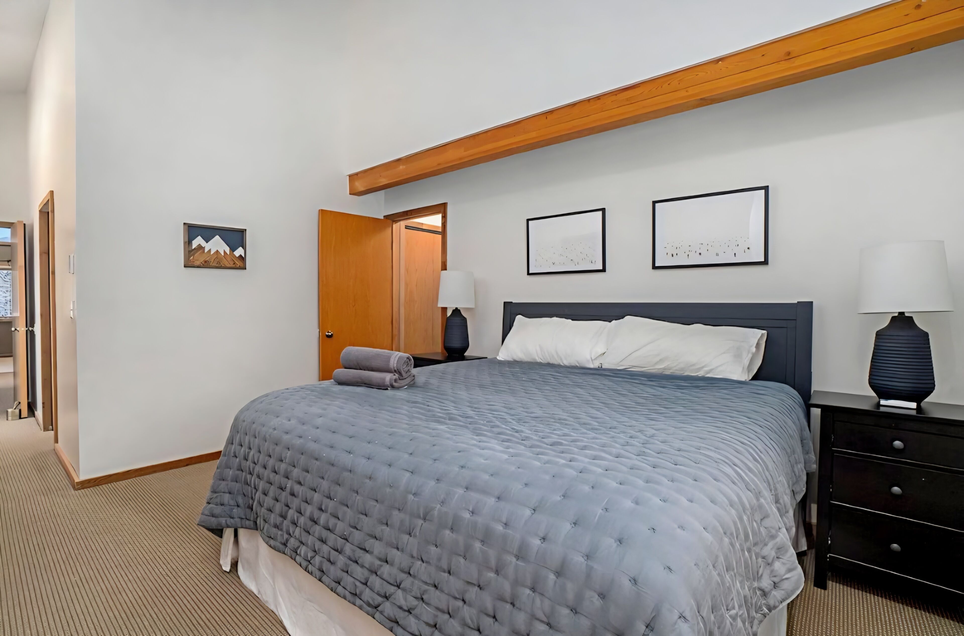 Ein Schlafzimmer mit einem Bett, zwei Nachttischen, einer Tür und zwei Wandbildern.