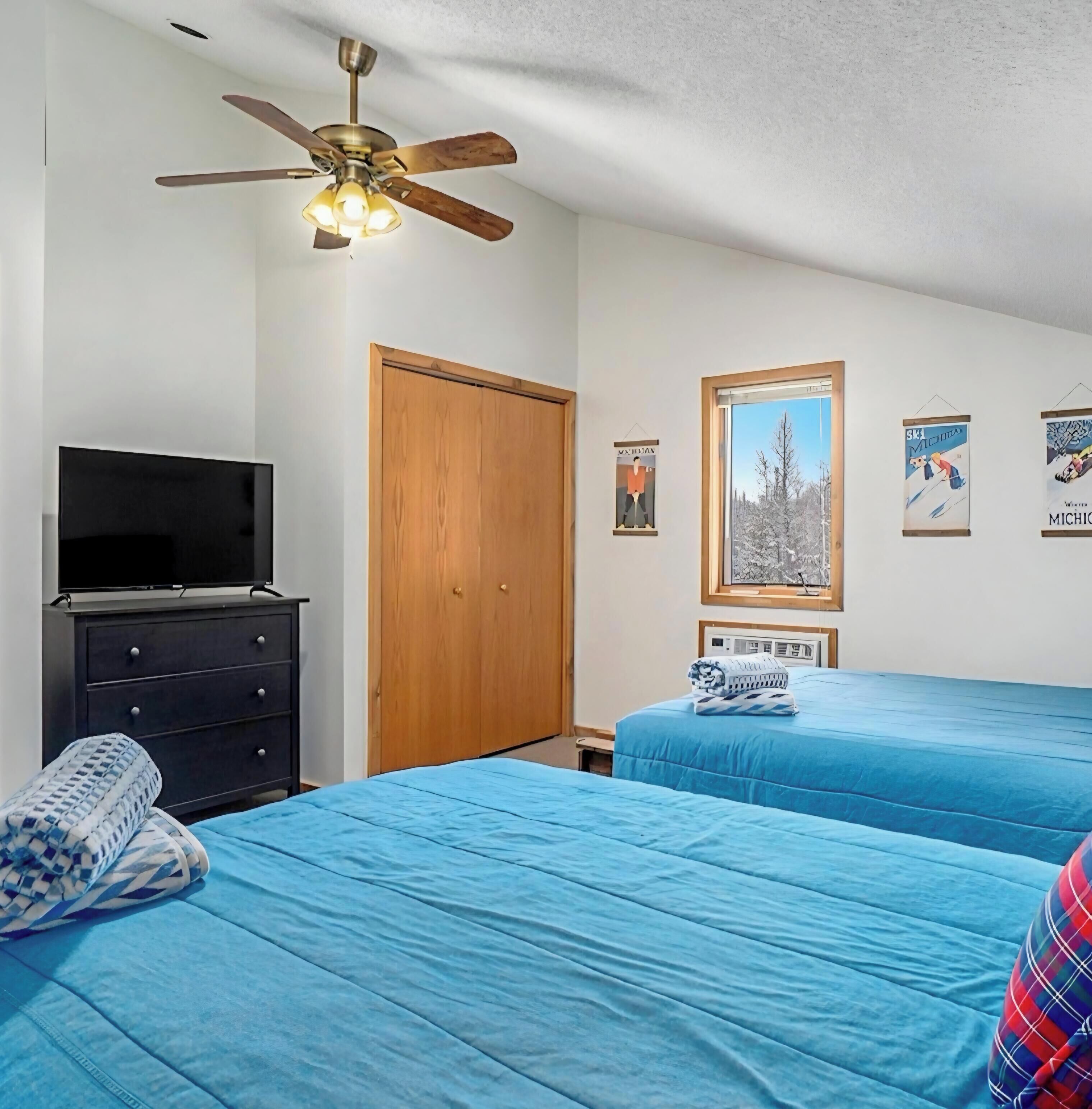 A bedroom with two beds, a ceiling fan, a TV, and a wardrobe.