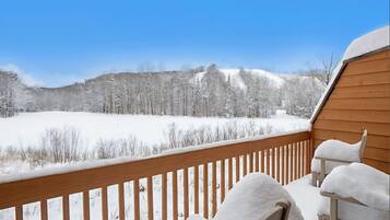 Um deck de madeira com cadeiras cobertas de neve e vista para uma paisagem nevada.