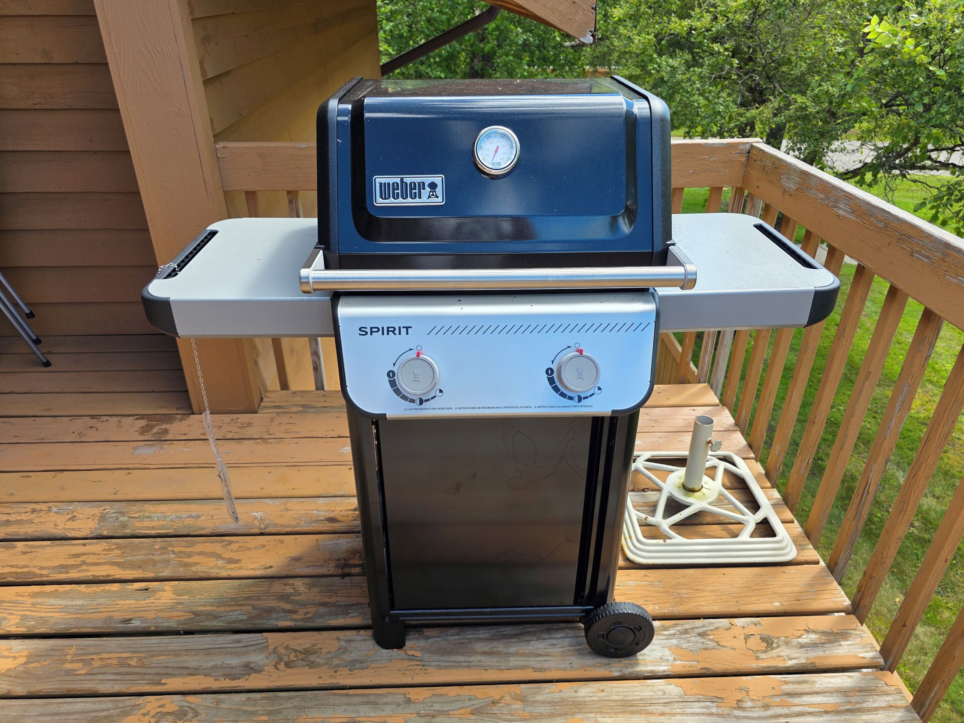 A Weber Spirit grill with a digital thermometer, placed on a wooden deck.