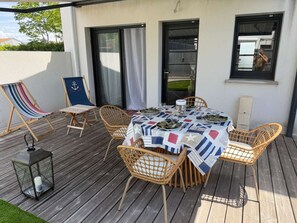 An outdoor patio with a table set for dining, surrounded by wicker chairs, and a lantern on the deck. - Maison climatisée avec jardin (BISCARROSSE)