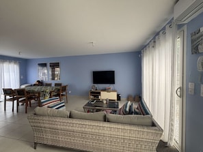 A living room with a sofa, a television, and a dining area with chairs and a table. - Maison climatisée avec jardin (BISCARROSSE)